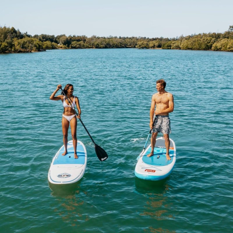 A Couple stand-up paddleboarding on calm blue water under a clear sky